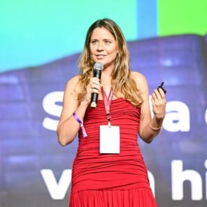 Psicóloga Mayra Gaiato de vestido vermelho segurando microfone durante palestra sobre autismo